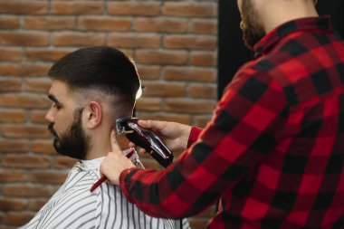 Saç kesimini mükemmel gösteriyor. Genç sakallı adam berber dükkanında sandalyede otururken kuaför tarafından tıraş oluyor.