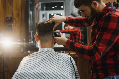 Saç kesimini mükemmel gösteriyor. Genç sakallı adam berber dükkanında sandalyede otururken kuaför tarafından tıraş oluyor.