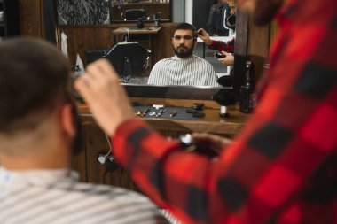 Saç kesimini mükemmel gösteriyor. Genç sakallı adam berber dükkanında sandalyede otururken kuaför tarafından tıraş oluyor.