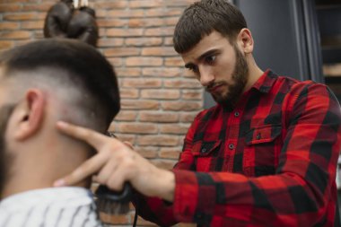 Saç kesimini mükemmel gösteriyor. Genç sakallı adam berber dükkanında sandalyede otururken kuaför tarafından tıraş oluyor.