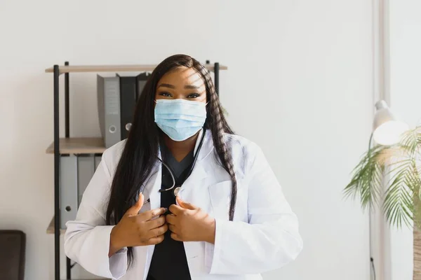 medicine, profession and healthcare concept - african american female doctor or scientist in protective facial mask in clinic