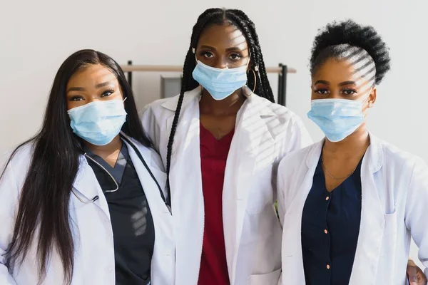 Group of healthcare workers wearing protective face masks while standing with arms crossed and looking at camera.