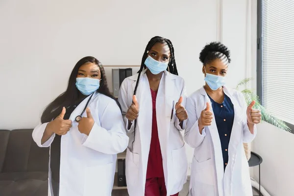 Group of healthcare workers wearing protective face masks while standing with arms crossed and looking at camera.