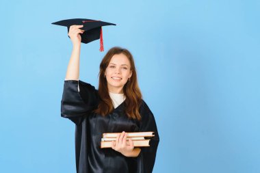 Mavi arka planda mezuniyet şapkası ve cübbesi giyen mezun bir kadın öğrenci.