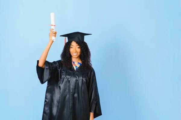 Young African-American student in bachelor robe on color background