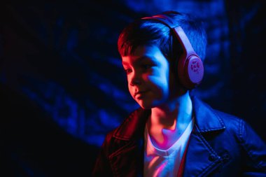 Stüdyo karanlık stüdyoda neon ışıkla çekiliyor. Kulaklıklı şık bir çocuğun portresi.