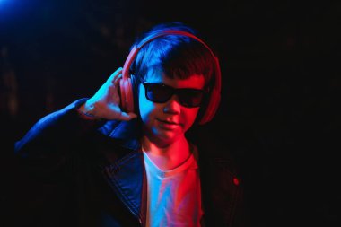 Stüdyo karanlık stüdyoda neon ışıkla çekiliyor. Kulaklıklı şık bir çocuğun portresi.