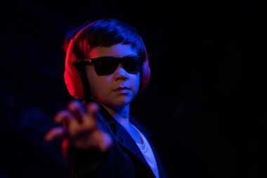 Kulaklıklı müzik dinleyen genç bir çocuk, neon ışıklı trend portresi. Kameraya bak.