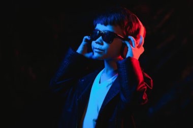 Stüdyo karanlık stüdyoda neon ışıkla çekiliyor. Kulaklıklı şık bir çocuğun portresi.