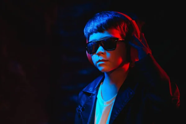 Studio shot in dark studio with neon light. Portrait of a stylish boy with headphones