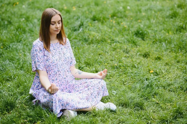 妊娠中の女性が公園でヨガをしています 草の上に座り — ストック写真