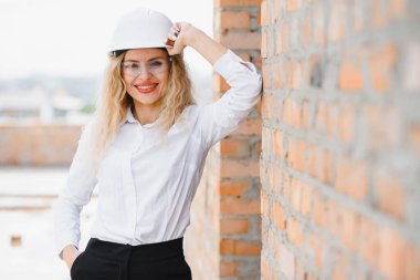 İnşaat mühendisi. İnşaat belgeleri olan bir kız. Binanın çatısına dayanmış beyaz şapkalı bir kadın. Yeni bir evin inşaatı.