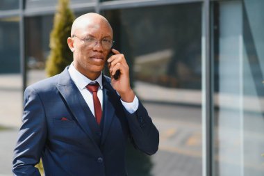 İş İletişimi. Şehir merkezinde neşeli bir Afro İş adamı telefon görüşmesi yapıyor. Boşluğu Kopyala