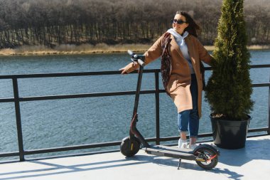 İşe elektrikli scooterla giden genç, güzel bir kadın, modern kız, yeni nesil, elektrik nakli, ekolojik ulaşım, ekolojik ulaşım, günbatımı, elektrikli kaykay.