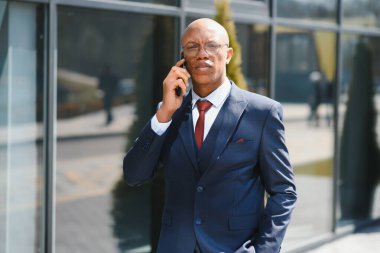 İş İletişimi. Şehir merkezinde neşeli bir Afro İş adamı telefon görüşmesi yapıyor. Boşluğu Kopyala