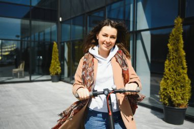 Genç bir kadın cep telefonuyla bir e-scooterın kilidini açıyor.