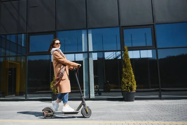 Fiatal Gyönyörű Kabátban Mosolyog Elektromos Robogóval Jár Irodaházakba Dolgozni — Stock Fotó