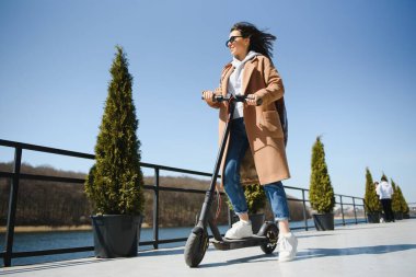 Şehirde elektrikli scooterlı genç bir kadın var.