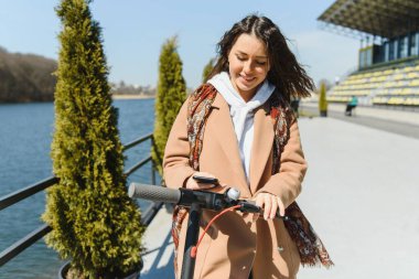 Genç bir kadın cep telefonuyla bir e-scooterın kilidini açıyor.