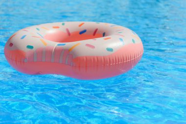 Hippi serpiştirilmiş donut, güneşli havuzun arka planında, parlak, berrak havuz suyunun üzerine serpilmiş.