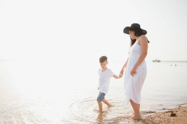 Mutlu anne ve oğlu sahilde yürüyor, aile denizde.