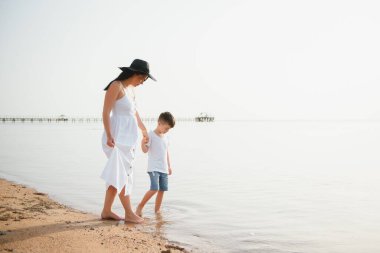 Anne ve oğlu gün batımında sahilde yürüyor.