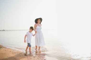 Mutlu anne ve oğlu sahilde yürüyor, aile denizde.