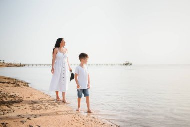 Anne ve oğlu gün batımında sahilde yürüyor.