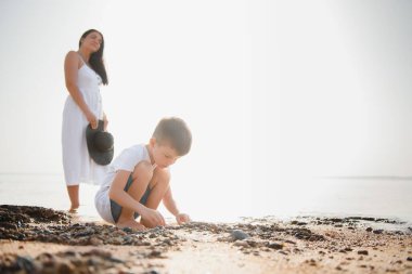 Anne ve oğlu gün batımında sahilde yürüyor.
