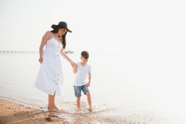 Anne ve oğlu gün batımında sahilde yürüyor.