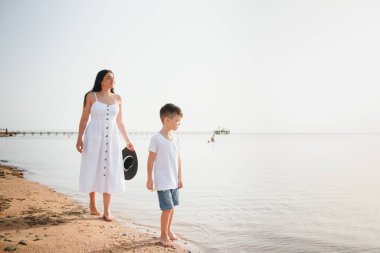 Anne ve oğlu gün batımında sahilde yürüyor.