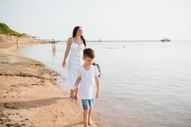 Anne ve oğlu gün batımında sahilde yürüyor.