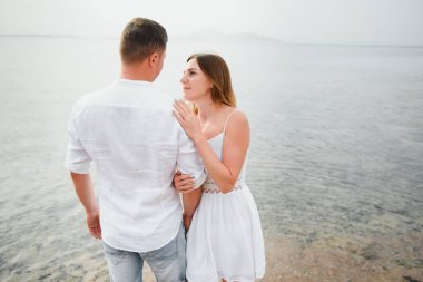 Kumsalda birlikte yürüyen tatilci çift birbirine sarılıyor. Mutlu ırklar arası genç çift, Asyalı kadın ve beyaz adam.