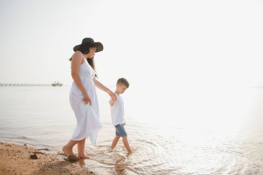 Mutlu anne ve oğlu sahilde yürüyor, aile denizde.