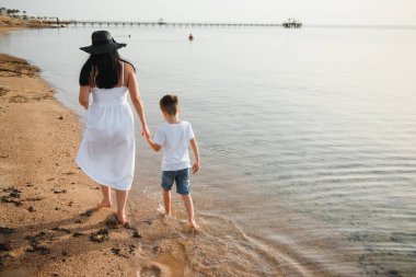 Mutlu anne ve oğlu sahilde yürüyor, aile denizde.