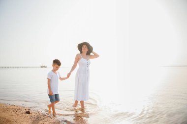 Anne ve oğlu gün batımında sahilde yürüyor.