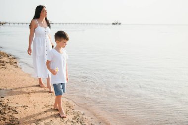 Anne ve oğlu gün batımında sahilde yürüyor.