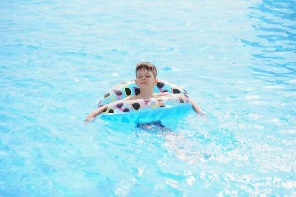 水泳プールで幸せな少年 少年は一人で 膨脹可能なリングを泳いでいて 水の飛沫に囲まれています ぬれたティーンエイジャーは遊園地で夏の週末を楽しんでいます コピースペース付きバナー — ストック写真