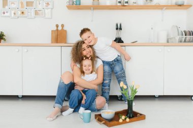 Mutlu genç bir aile, çocuklu bir anne yeni modern tasarım mutfağında sıcak ahşap zemine oturur, heyecanlı küçük çocukları olan bir anne dinlenir yenilenmiş bir dairede dinlenir, konsept taşınır.