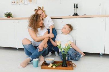 Modern mutfağın ahşap zemininde oturan mutlu anne ve oğul kucaklaşması. Anne çocukları kucaklıyor. Mutlu aile ilişkileri konsepti