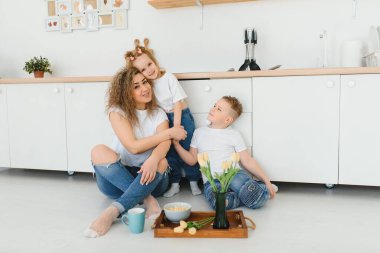 Modern mutfağın ahşap zemininde oturan mutlu anne ve oğul kucaklaşması. Anne çocukları kucaklıyor. Mutlu aile ilişkileri konsepti