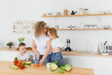 Genç anne ve iki çocuğu sebze salatası yapıyor.