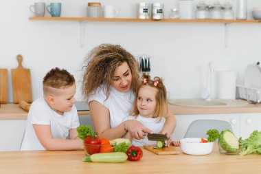 Genç anne ve iki çocuğu sebze salatası yapıyor.