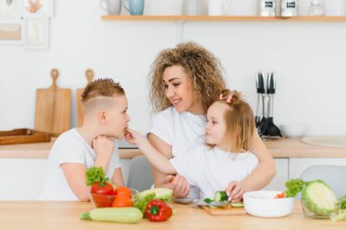 Genç anne ve iki çocuğu sebze salatası yapıyor.