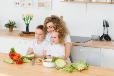 Genç anne ve iki çocuğu sebze salatası yapıyor.