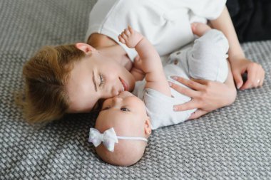 Genç ve mutlu anne, yeni doğmuş bebeğini kucaklıyor. Sabahları yatakta oturuyor..