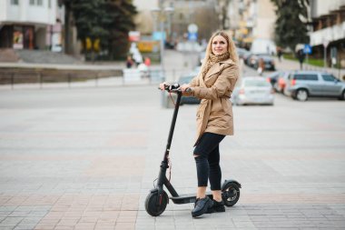 Şehirde elektro scooter kullanan genç bir kadın..