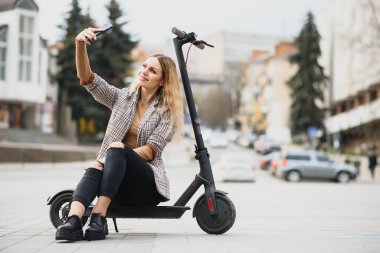 Şehirde elektro scooter kullanan genç bir kadın..
