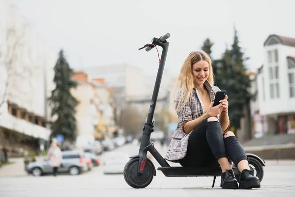 Beautiful young woman sitting on her electro scooter .