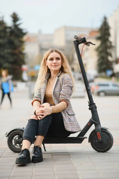 young woman on electro scooter in city. woman riding scooter in sunset light in street